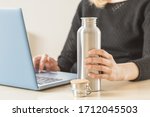 White woman holding her personal stainless steel water bottle on the working table. Daily hydration habit to stay healthy