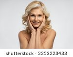 Isolated portrait on white background of charming attractive 50 years mature woman with blond shiny hair, holding hands on her face and smiling toothy smile looking at camera. Beauty treatment concept