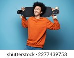 Young smiling African American man holding longboard isolated on blue background. Portrait of attractive happy skater looking at camera. Street culture, active lifestyle concept 