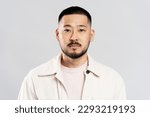 Small photo of Portrait of handsome serious asian man with stylish hair, wearing casual clothes, looking at camera after barbershop service, isolated on white background