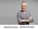 Emotional studio portrait of handsome confident elderly senior gray haired man in casual clothes, posing with his arms crosse, smiling looking away at copy advertising space, isolated grey background