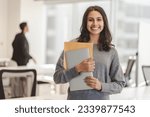 Small photo of Smiling confident Indian woman wearing casual clothes holding laptop and documents, looking at camera at modern office. Good looking businesswoman posing for picture. Concept of successful business