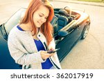 Young woman standing next to car using mobile phone and smiling - Red hair young girl having fun using smartphone technology - Concept of success and leisure soft focus due halo of the solar flare 