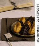 Small photo of Madeleine cookies with chocolate glaze on the ceramic plete, brown linen cloth, opened book on the background