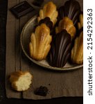 Small photo of Madeleine cookies with chocolate glaze on the ceramic plete, brown linen cloth, pieces of chocolate and cookie