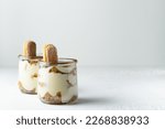 Traditional italian dessert tiramisu with savoiardi biscuits, mascarpone cheese, cream, egg yolks, amaretto liqueur, coffee and cocoa. Portion serving in glass jars. White background, copy space