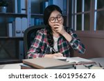 Small photo of Young woman student at home desk reading and yawning tired at night with pile of books. exhausted college girl preparing exam in midnight stay up late hard working. university education concept