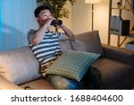 Small photo of Young asian chinese man watching television drinking bottle of beer in late evening time. handsome guy enjoy alcohol alone in sofa at night in apartment. single male stay up late relax on couch
