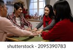 Small photo of asian family members looking at each other with sly smiles while shuffling mahjong pieces on the table. staying up playing tile game on chinese new year eve at home