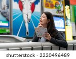 Asian girl holding map leaning on railing with hand on chin while thinking about where to go next with glico man sign at background in shinsaibashi suji and doutonbori Osaka japan