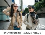 two smiling asian chinese female coworkers chatting happily on pedestrian walk while walking to work together in san Francisco California usa.