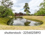 Small photo of Kyoto, Japan - April 18, 2018: the phoenix hall of Byodoin Temple at distance and lake water surrounded by green meadowland on a sunny day in uji at springtime