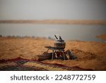 Small photo of An old copper jug ​​cooking tea on a fire in the desert of Saudi Arabia, with a view of Wadi Al-Rumah