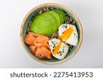 Small photo of Poke bowl with quinoa, salmon, avocado and two poached eggs. Round blue ceramic bowl isolated on white background. Yolks spread Top view.