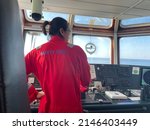 Small photo of a long-haired male sailor wearing a red coverall was piloting the ship, maneuvering the ship to dock. a seafarer under controlling vessel due to maneuver for alongside at jetty