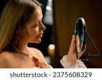 Small photo of portrait of a young beautiful needlewoman trying on a pearl necklace flaunting herself in mirror craft production hobby beauty