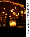 Dark background with burning glass candle and golden bokeh. Candlelight with fairy lights bokeh in front of cocktail bar. One candle flame light at night with bokeh on dark background.