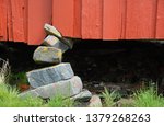 Small photo of Red house kept up by shaky foundation. Close up. Fundament of stacked stones.