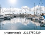 Small photo of La Savina harbour, on the island of Formentera (Balearic Islands, Spain). Yachts and sailboats moored and the port's commercial promenade, with a line of palm trees, in the background