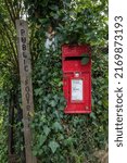Small photo of NETHER STOWEY, UK - 23 AUGUST 2017: A village post box surrounded by ivy next to a sign for a public footpath.