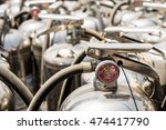 Small photo of Close up of the guage of a depressurized discarded old silver fire extinguisher standing with others abandoned in the sun.