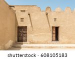 The inner courtyard of a restored traditional old Arabian building in strong sunlight with shadows from wooden gutters and carved wooden doors and window lattices for ventilation.