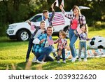 large american family spending time together. With USA flags against big suv car outdoor. America holiday. Four kids.