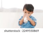 Small photo of A 1 year and 5 month old boy is sitting drinking milk from a glass on a white carpet under the concept of drinking milk for a healthy body and growing up.
