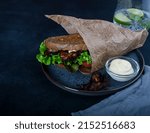 Small photo of btl sandwich on a black plate in brown parchment on a dark background with copy space