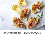 Small photo of Appetizer crostini, tapas, open faced sandwiches with pear, prosciutto, arugula and blue cheese on white marble board. Delicious snack, appetizers