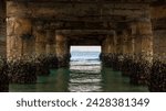 Small photo of Perspective of the blue water from the coast beneath the concrete pier. View of the turquoise sea at the coast from beneath the concrete pier.