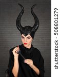 Small photo of Maleficent demonic - starring. Beautiful woman from a fairytale with hair horns indoor. Beautiful girl with horns dressed up as devil. Woman with makeup, nail polish. Fantasy. Halloween concept.