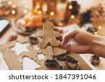 Person holding gingerbread man cookie, Christmas holiday advent. Hand cutting gingerbread dough with christmas man metal cutter on background of festive lights, decorations on rustic table
