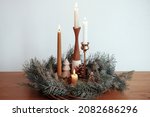 Christmas advent. Stylish candles burning in christmas wreath with pine cones and tree decor on wooden table on background of white wall in modern festive room. Atmospheric winter holidays time