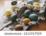 Small photo of Happy Easter! Easter eggs on rustic table with cherry blossoms. Natural dyed colorful eggs on linen napkin and spring flowers in rustic room. Countryside still life. Atmospheric image