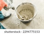 Worker mixing gypsum plaster with water for plastering walls. Construction of house and home renovation concept. Close up of bucket with stucco mix and handyman hands