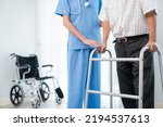 Physiotherapist assists her contented senior patient on folding walker. Recuperation for elderly, seniors care, nursing home.