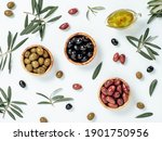 Small photo of Set of green olives, black olives and red kalmata olives and extra virgin olive oil on white background. Top view of different types of olives in bowls and oil on leaves and branches background.