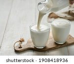 Small photo of Pouring homemade kefir, buttermilk or yogurt with probiotics. Yogurt flowing from glass bottle on white wooden background. Probiotic cold fermented dairy drink. Trendy food and drink. Copy space left