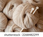 Small photo of Aesthetic image of beige light, airy yarn skein. Close up view of medium thick blow yarn made of baby alpaca and merino wool. Knitting needles stuck in skein of yarn. Copy space