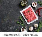 Fresh raw minced beef on backing paper and cutting board and ingredients over black cement background with copy space. Top view or flat-lay.