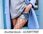 Close-up fashion portrait of young stylish hipster girl posing at city street,stylish woman's look,wool blue jacket,grey sweater and trendy jean shorts party,toned colors,soft vintage