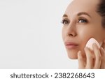 Small photo of Closeup portrait of a woman applying dry cosmetic tonal foundation using makeup sponge on the face using makeup brush.