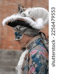 Small photo of Venice, Italy - 02.19.2022: A middle-aged man in a vintage costume with a lace collar, wearing a carnival mask, tricorn hat with feathers, stands in profile at the carnival in Venice, Italy