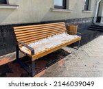 Wooden bench under snow and a trash can next to a house in Moscow