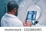 Small photo of African American doctor examine scan attentively. Medical worker shooted from back. Male doctor examines MRI scan. Multicultural doctor is scrolling screen of tablet with scans of brain.