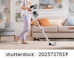 Young woman uses cordless vacuum cleaner to clean home carpet. Modern easy cleaning.