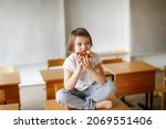 Small photo of Cute caucasian girl child blonde eating a piece of pizza with cheese sitting on the table, a snack in kindergarten, junk food and fast food for children, ill-mannered children with bad habits