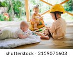 Small photo of Three European sibling children play side by side on wooden porch. Newborn baby with older brother and sister. Summer in backyard, eco-friendly wooden safe toys