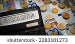 Small photo of Tax exemption in France and Canada. Calculator with the words "defiscalisation" in French. In the background there are many euro bills and coins. The concept of the need to pay taxes annually